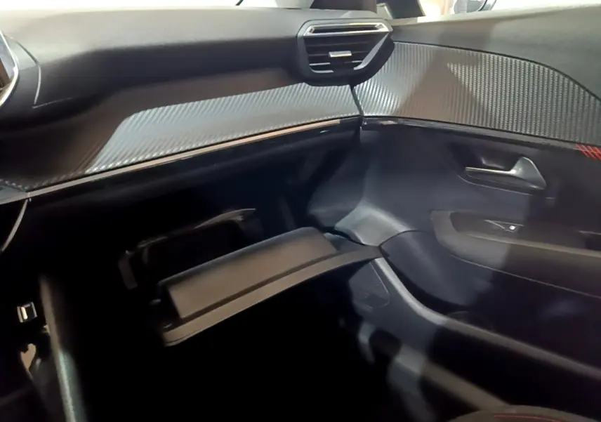 Vue intérieure côté passager de la Peugeot 208 noire, avec boîte à gants ouverte et tableau de bord texturé gris.