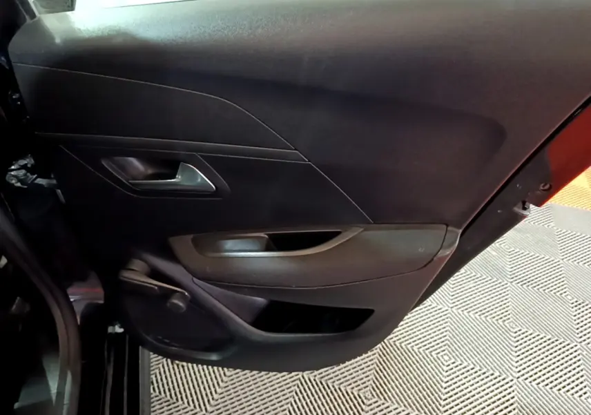 Vue rapprochée de la porte arrière gauche noire d’une Peugeot 208 avec poignée intérieure argentée et rangement intégré.