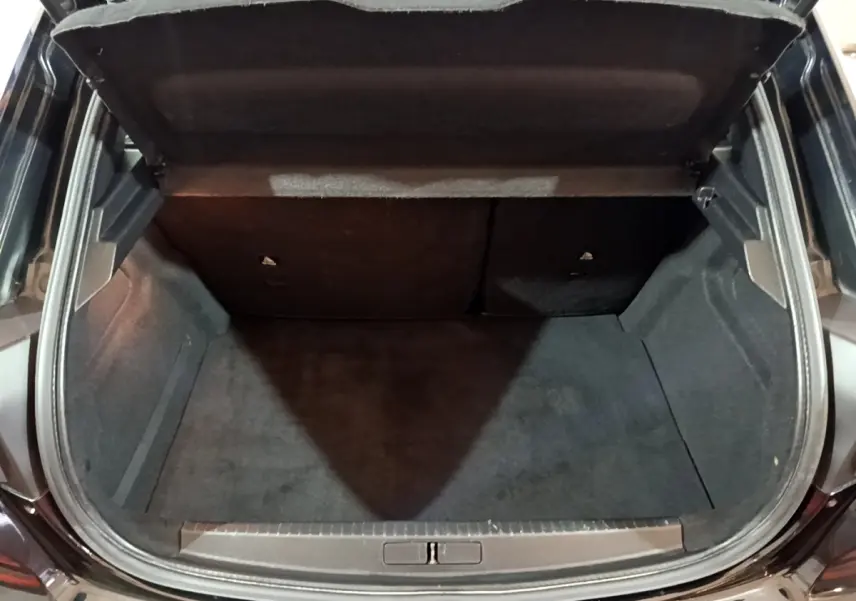 Coffre ouvert vu de l'arrière d'une Peugeot 208 noire, intérieur spacieux et revêtement sombre.