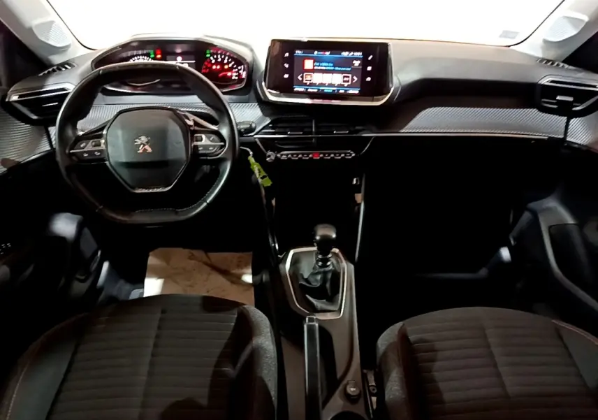 Vue intérieure frontale du tableau de bord noir de la Peugeot 208 avec volant cuir, écran tactile central et boîte manuelle.