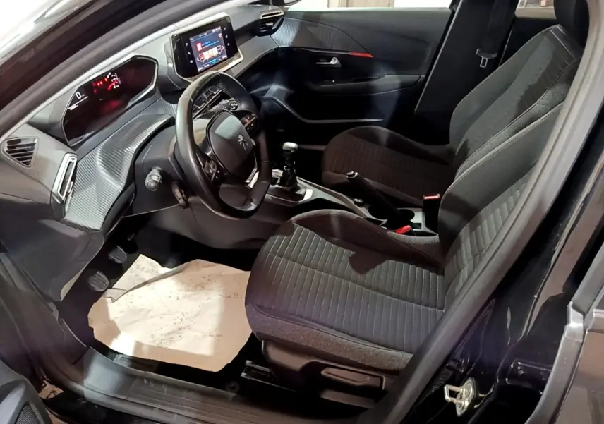 Vue intérieure côté conducteur de la Peugeot 208 noire, montrant le tableau de bord avec écran tactile et volant cuir multifonctions.