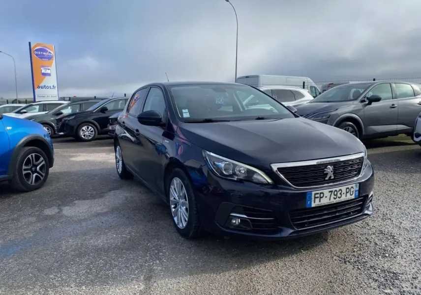 Peugeot 308 bleu foncé vue 3/4 avant droit sur parking avec calandre chromée et phares LED.