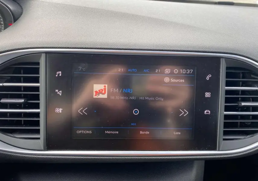 Écran tactile central de la Peugeot 308 2018 affichant la radio FM NRJ, entouré de grilles d'aération noires.