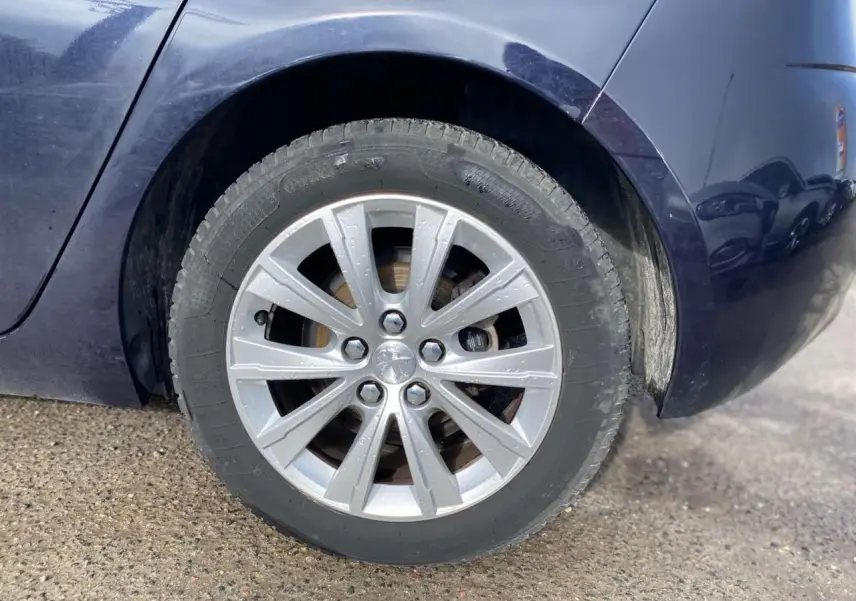 Gros plan sur la roue arrière droite d'une Peugeot 308 bleu foncé, avec jante alliage et carrosserie métallisée visible.