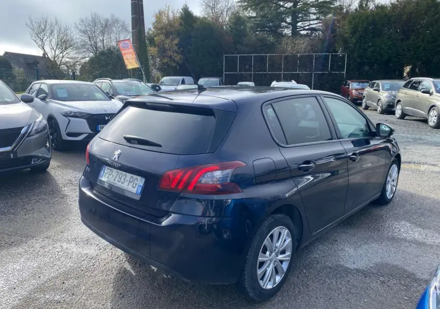 Peugeot 308 bleu foncé vue 3/4 arrière droit, avec feux arrière LED et jantes alliage visibles.