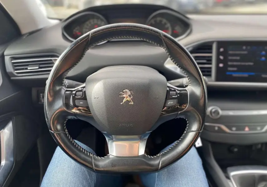 Vue intérieure centrée sur le volant cuir noir de la Peugeot 308 2018 avec tableau de bord et écran tactile visible.