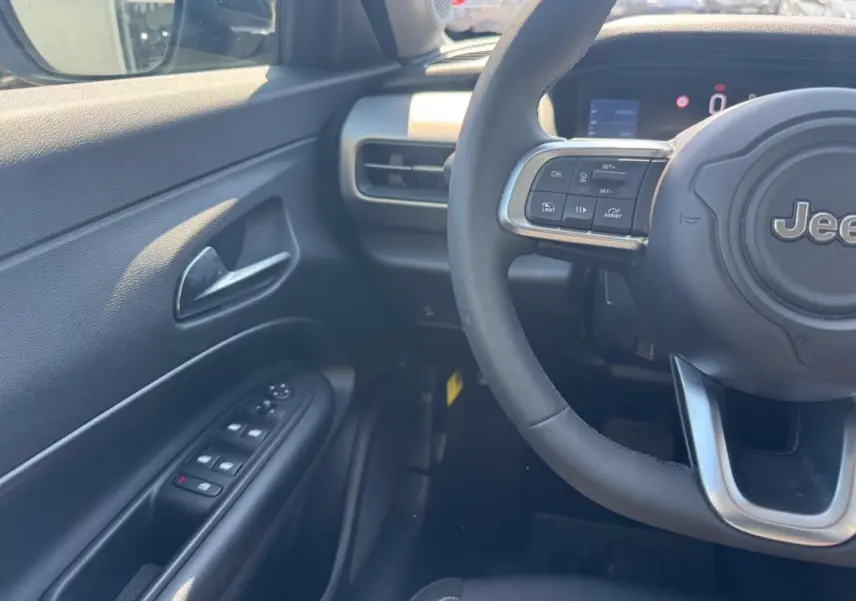 Vue intérieure côté conducteur du Jeep Avenger électrique blanc 2025, volant cuir et commandes au volant visibles.