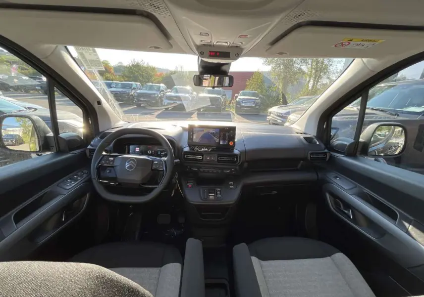 Vue intérieure avant du Citroën Berlingo 2026, tableau de bord noir avec écran tactile et sièges tissu gris et noir.