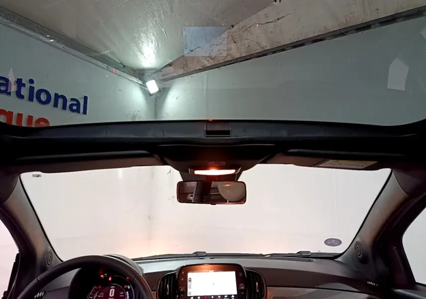 Vue intérieure avant de la Fiat 500 gris foncé 2022, avec tableau de bord numérique et toit panoramique ouvert.