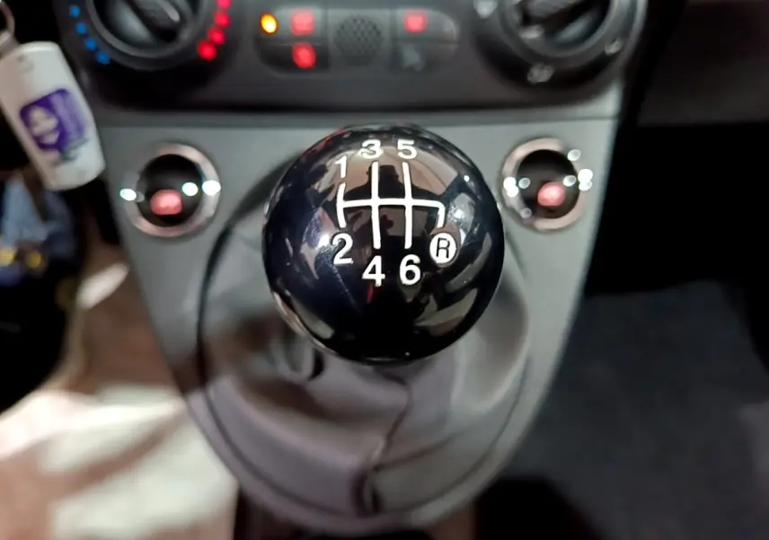 Gros plan sur le levier de vitesses manuel noir de la FIAT 500 gris foncé, avec tableau de bord en arrière-plan flou.