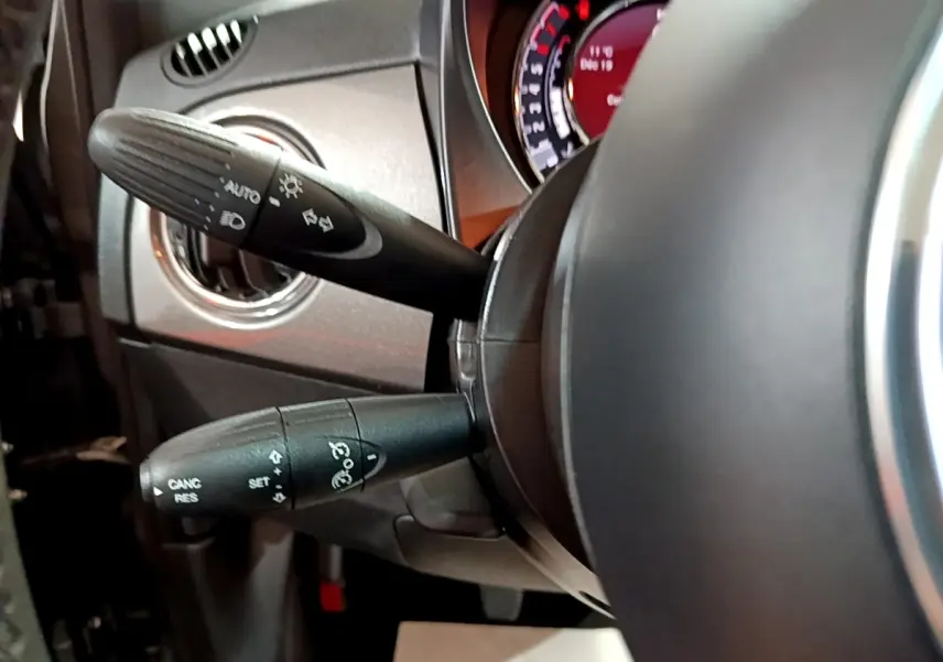 Gros plan sur les commandes au volant d'une FIAT 500 gris foncé, montrant les leviers de clignotants et régulateur.