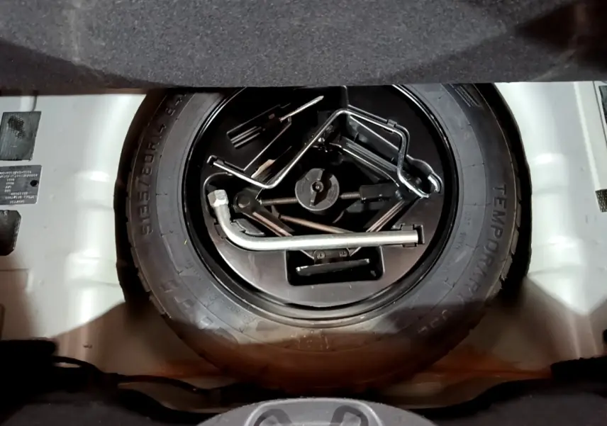 Gros plan sur la roue de secours et les outils de bord dans le coffre d'une Fiat 500 gris foncé, vue de dessus.