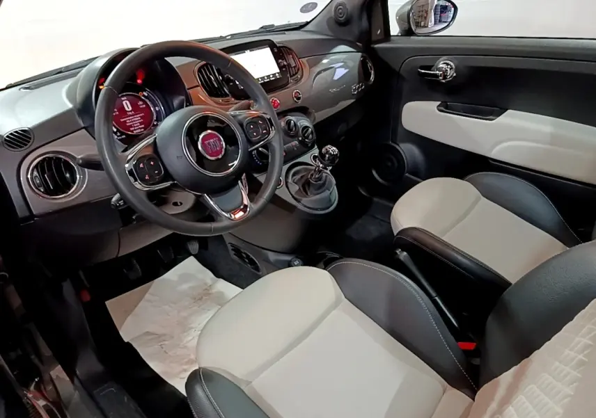Vue intérieure avant droite de la Fiat 500 1.0 Dolcevita avec tableau de bord gris brillant et sièges bicolores beige et noir.