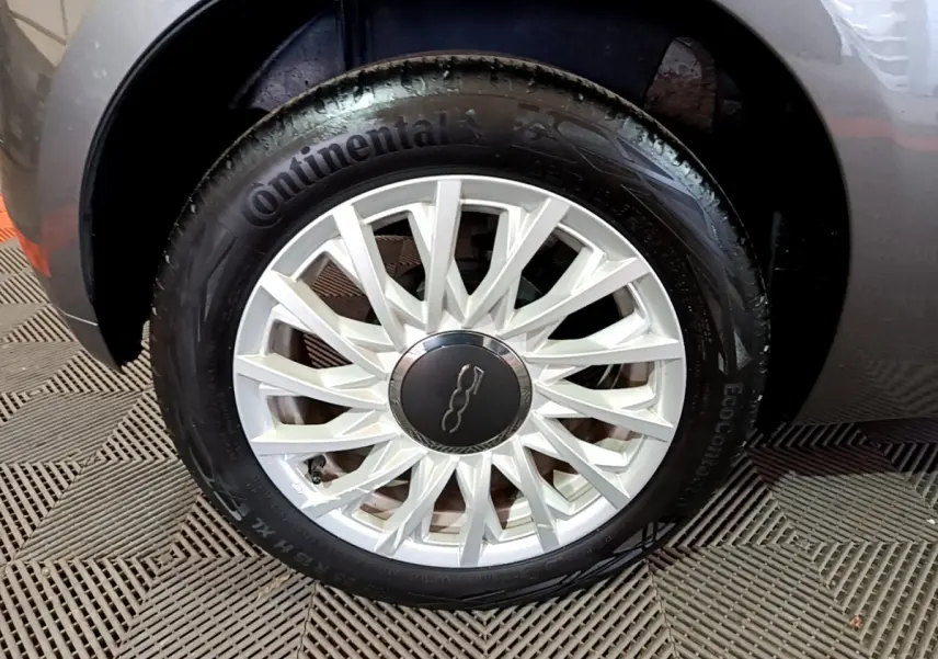 Gros plan sur la roue avant gauche grise d'une FIAT 500 1.0 70ch BSG Dolcevita avec jante argentée à rayons fins.