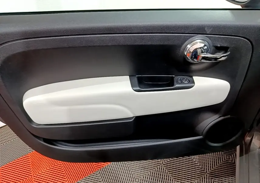 Gros plan sur la porte intérieure côté conducteur de la Fiat 500 gris foncé, avec poignée chromée et insert beige clair.