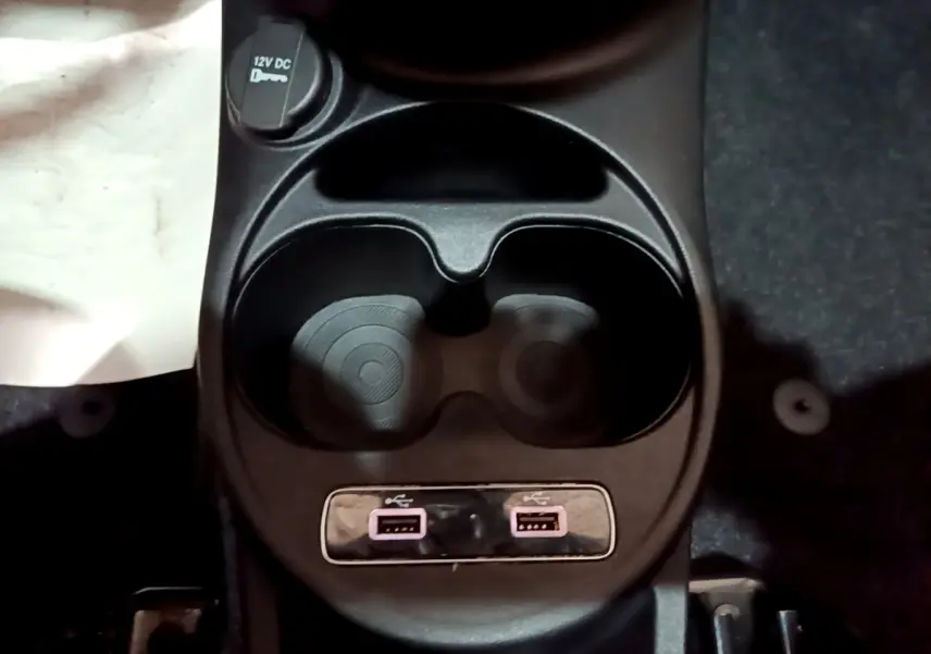 Gros plan sur la console centrale noire de la Fiat 500 avec porte-gobelets, prise 12V et deux ports USB.