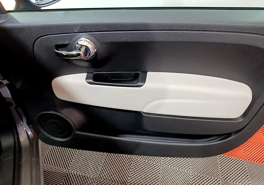 Vue intérieure côté gauche de la porte d’une Fiat 500 gris foncé avec poignée chromée et panneau beige.