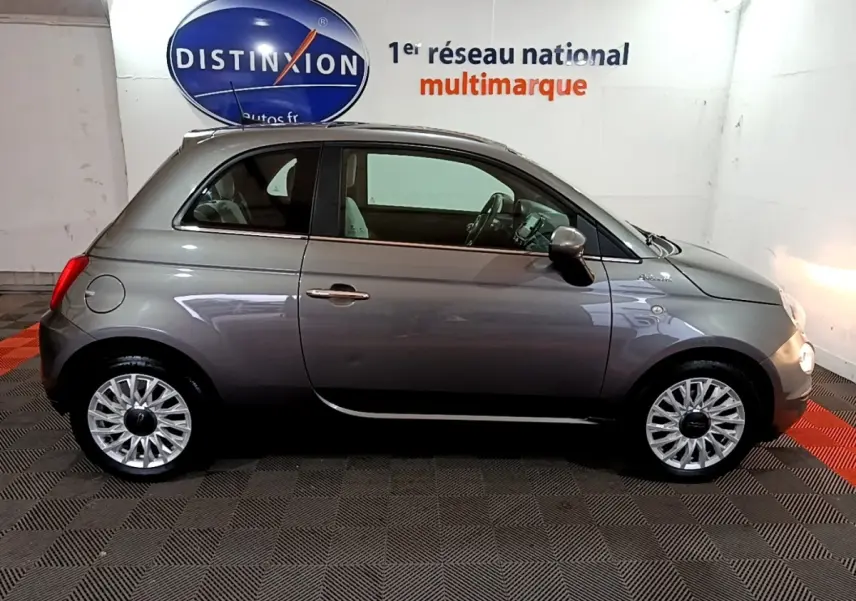 Profil droit d'une FIAT 500 gris foncé 2022 avec jantes alliage et intérieur clair visible en arrière-plan showroom.