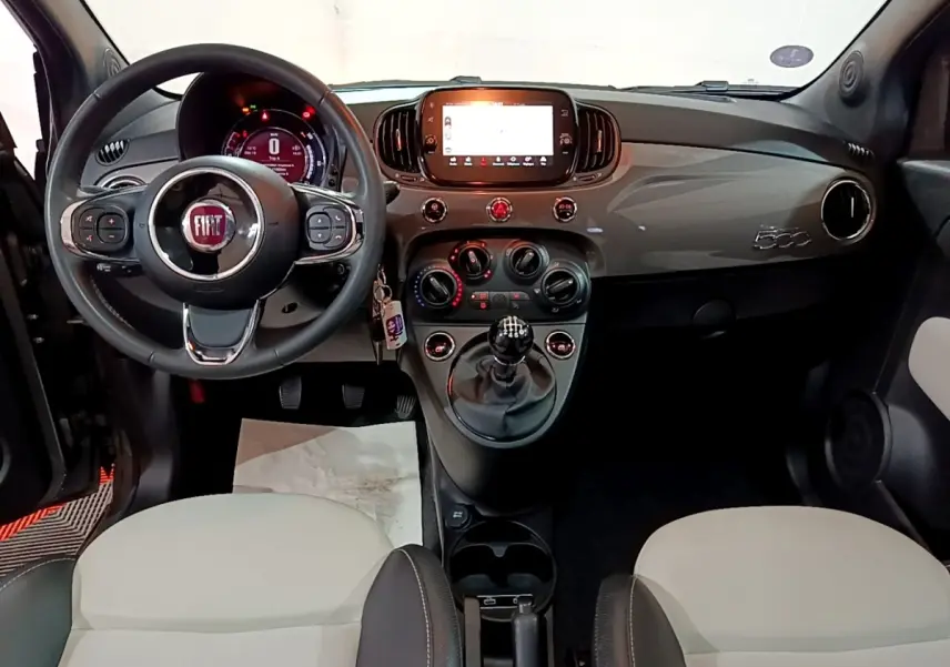 Vue intérieure avant de la Fiat 500 gris foncé 2022, volant cuir, tableau de bord avec écran tactile et boîte manuelle.