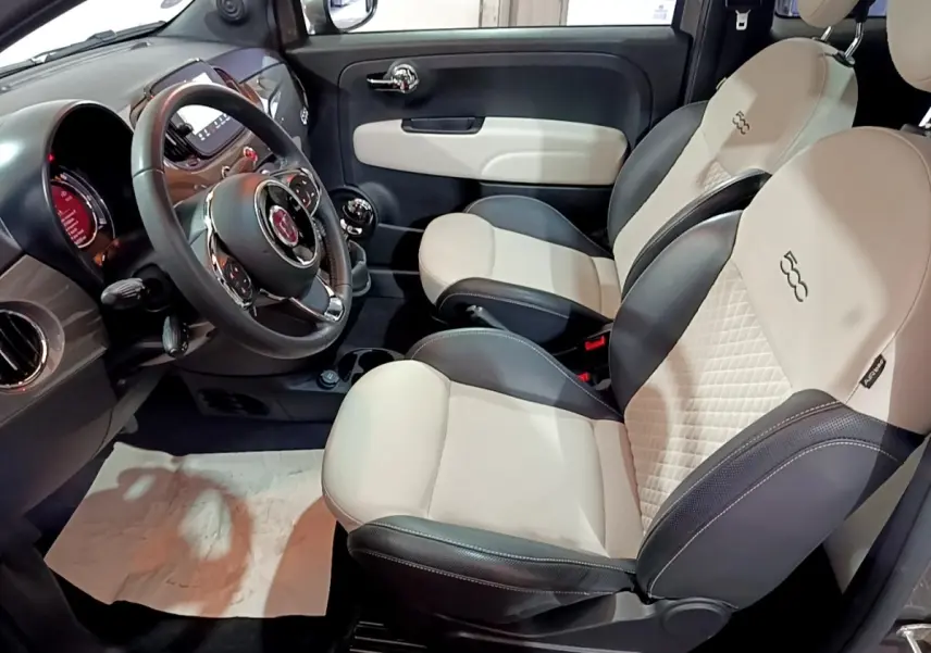 Vue intérieure côté conducteur de la Fiat 500 1.0 gris foncé, sièges bi-ton beige et noir avec logo 500 brodé.