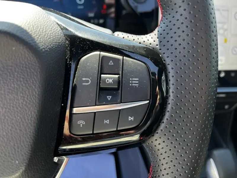 Gros plan sur les commandes multifonctions côté gauche du volant perforé noir avec surpiqûres rouges du Ford Puma blanc 2025.