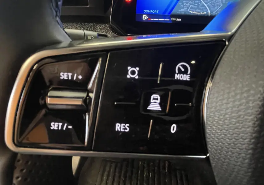 Gros plan sur les commandes au volant gauche de la Renault Clio VI gris Rafale, avec affichage digital en arrière-plan.