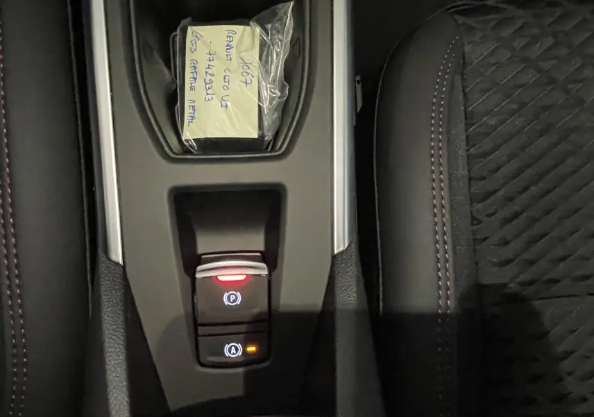 Gros plan sur la console centrale d’une Renault Clio VI gris Rafale, avec boutons de frein à main et auto hold éclairés.