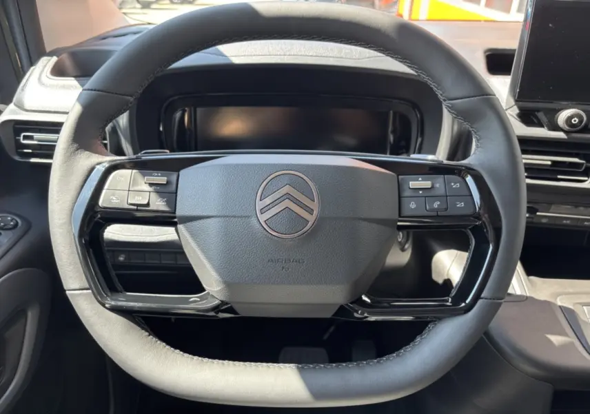 Vue rapprochée du volant cuir multifonctions noir du Citroën Berlingo 2026, avec tableau de bord et écran tactile en arrière-plan.