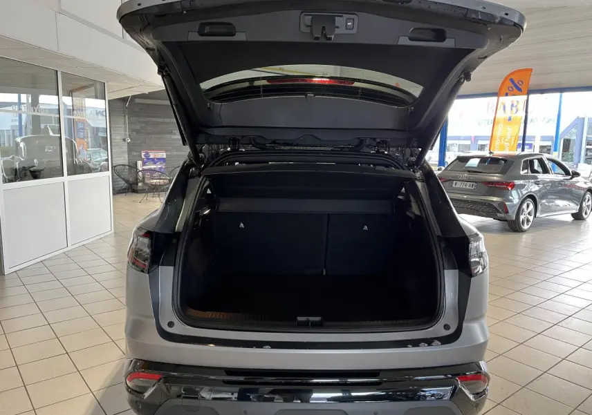 Vue arrière du Renault Austral gris avec hayon motorisé ouvert, montrant le coffre spacieux en intérieur showroom.