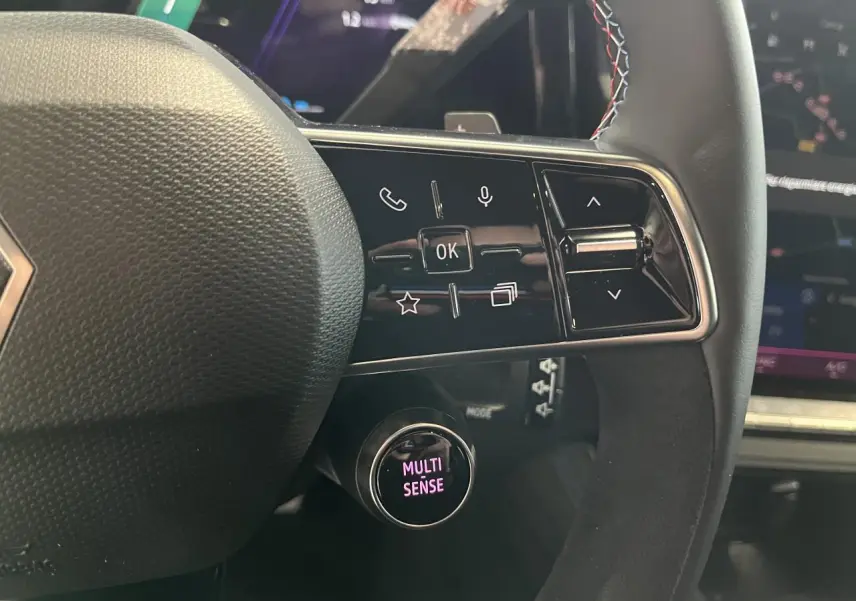 Gros plan sur le volant Alcantara du Renault Austral gris, avec commandes multifonctions et bouton Multi-Sense éclairé.