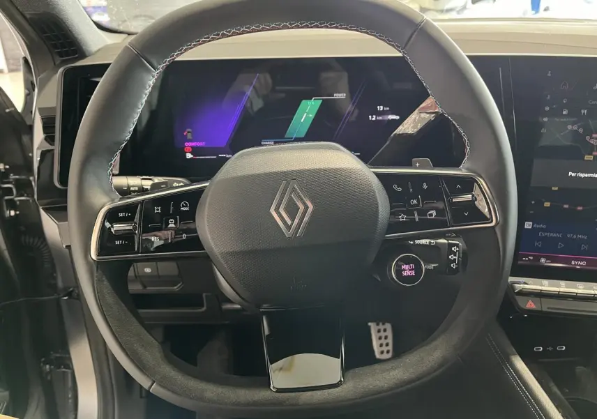 Vue rapprochée du volant en textile et Alcantara avec logo Renault, tableau de bord numérique et écran tactile du Renault Austral 2025.