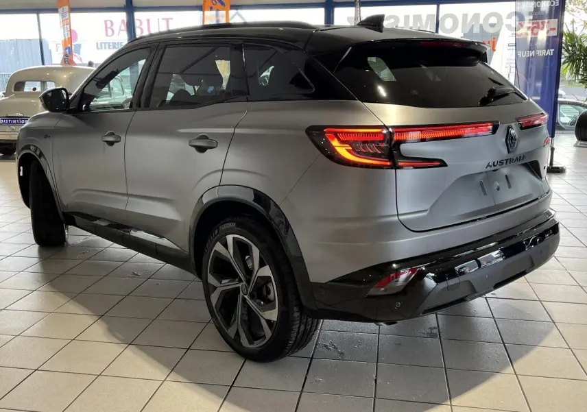 Vue 3/4 arrière droite du Renault Austral gris avec feux LED allumés et jantes alliage 20 pouces en intérieur showroom.