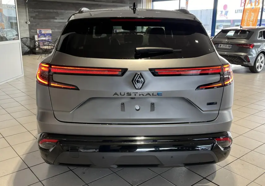 Vue arrière du Renault Austral gris avec feux LED allumés et hayon motorisé dans un showroom.