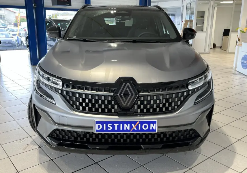 Vue de face du Renault Austral gris avec calandre à damier noire et logo noir, en intérieur showroom.
