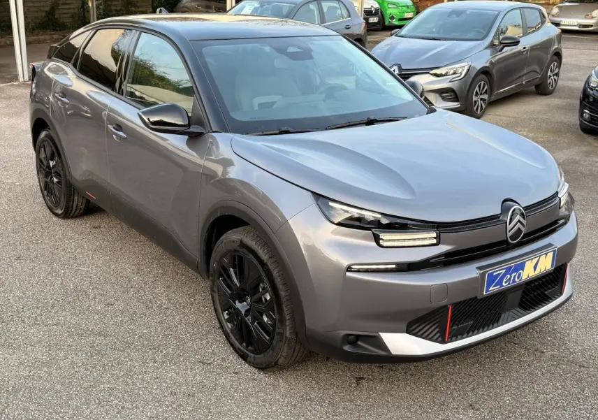 Vue 3/4 avant gauche d'une Citroën C4 hybride 2025 gris Mercury avec jantes noires et signature lumineuse LED distinctive.