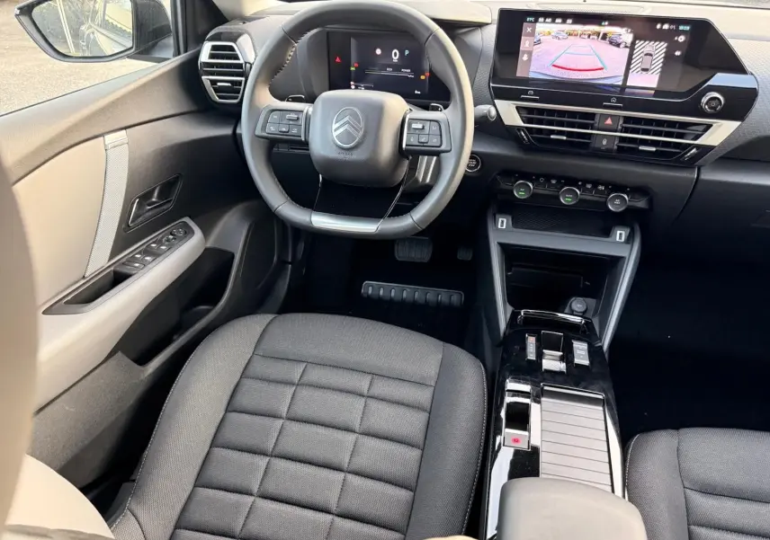 Vue intérieure avant centrée sur le volant et la console centrale noire du Citroën C4 hybride 2025 avec écran tactile affichant la caméra de recul.
