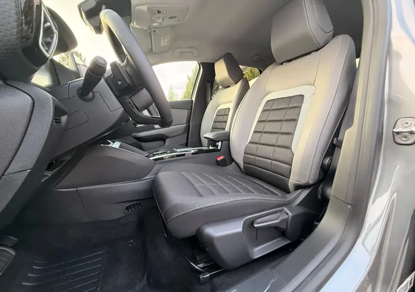 Vue intérieure côté conducteur de la Citroën C4 hybride gris Mercury, mettant en valeur les sièges bi-matière et le volant moderne.