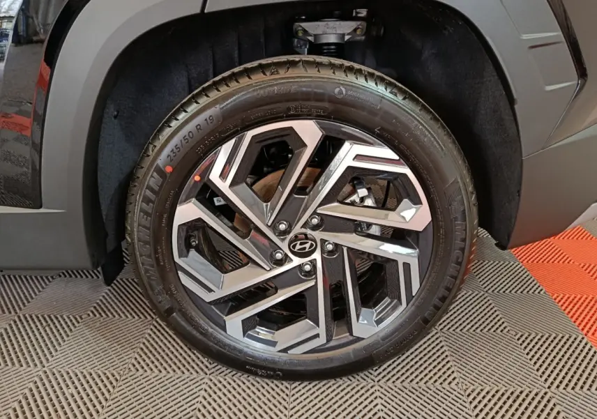 Gros plan sur la roue avant droite noire du Hyundai Tucson 2025, mettant en valeur la jante alu au design géométrique.
