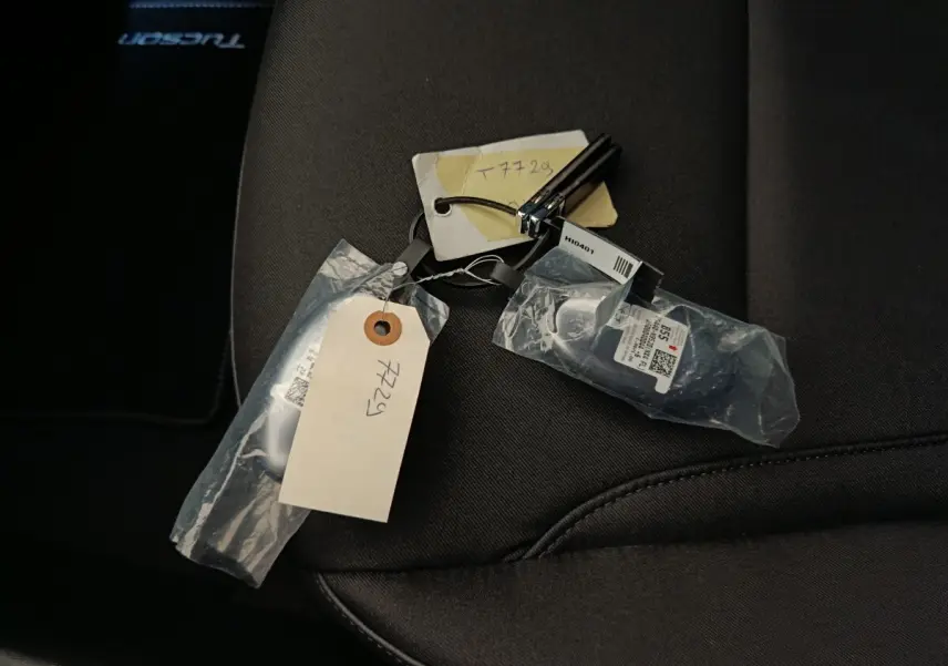 Clé de voiture Hyundai Tucson 1.6 Hybrid posée sur siège tissu noir avec tapis marqué Tucson visible en arrière-plan.