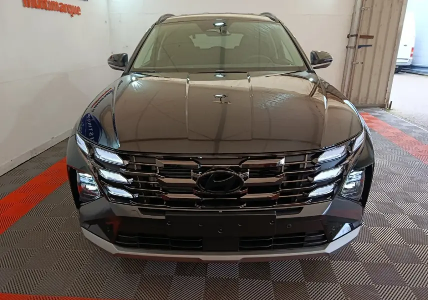 Vue avant d’un Hyundai Tucson 2025 noir avec calandre chromée et feux LED allumés en intérieur showroom.