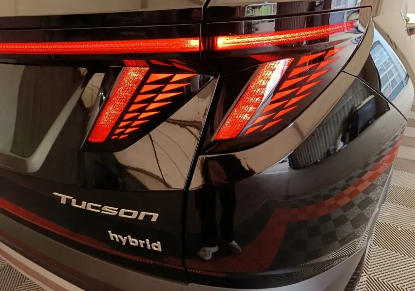 Gros plan sur le feu arrière droit rouge du Hyundai Tucson noir hybride avec logo et nom du modèle visibles.