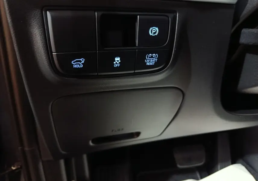 Gros plan sur les commandes noires sous le tableau de bord côté gauche du Hyundai Tucson 1.6 Hybrid 239 Creative Auto 2025.
