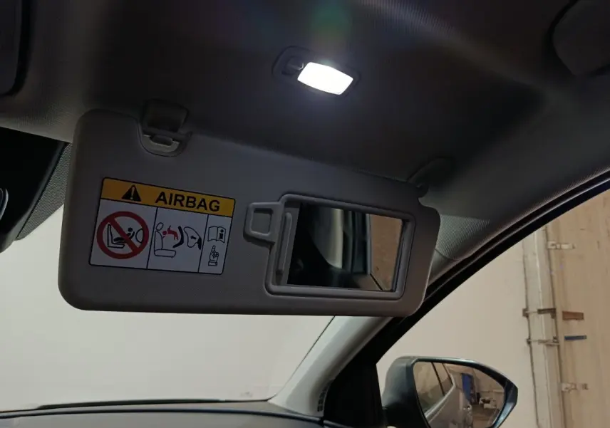 Détail intérieur du pare-soleil côté conducteur avec miroir et avertissement airbag, vue vers le rétroviseur noir.