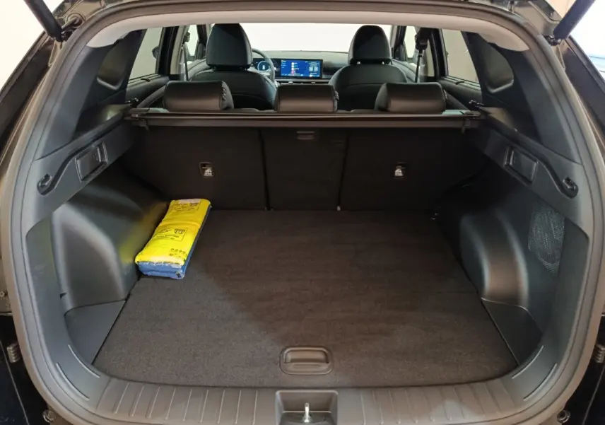 Coffre ouvert vu de l'arrière d'un Hyundai Tucson noir 2025, avec tablette cache-bagages et écran tactile visible.