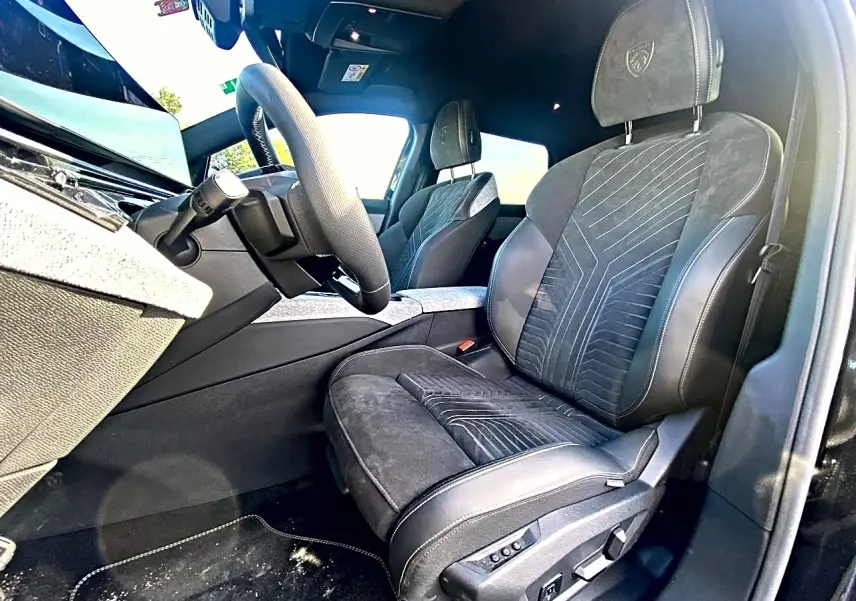 Vue intérieure côté conducteur du Peugeot 5008 Hybrid 145 GT e-dcs6 2025, sièges noirs avec surpiqûres et logo Peugeot brodé.