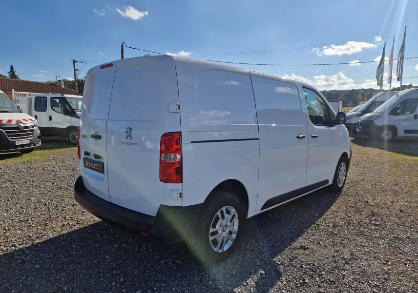 Peugeot Expert Fourgon blanc vu en 3/4 arrière droit sur un terrain extérieur ensoleillé avec plusieurs utilitaires autour.