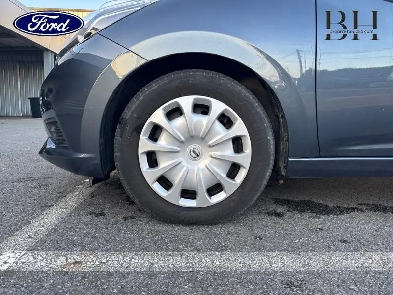 Gros plan sur la roue avant gauche d'une Nissan Micra gris acier avec enjoliveur et partie de l'aile avant visible.