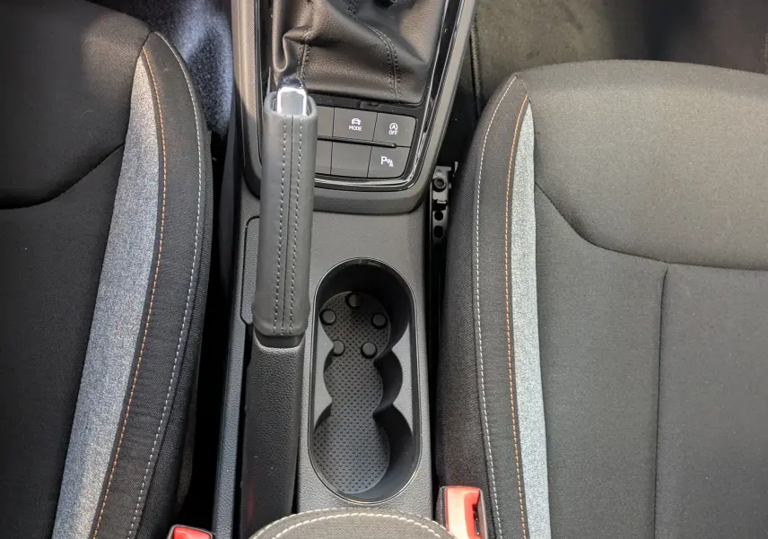 Vue plongeante sur la console centrale du Skoda Kamiq 2025 avec frein à main, porte-gobelets et sièges tissu gris et noir.