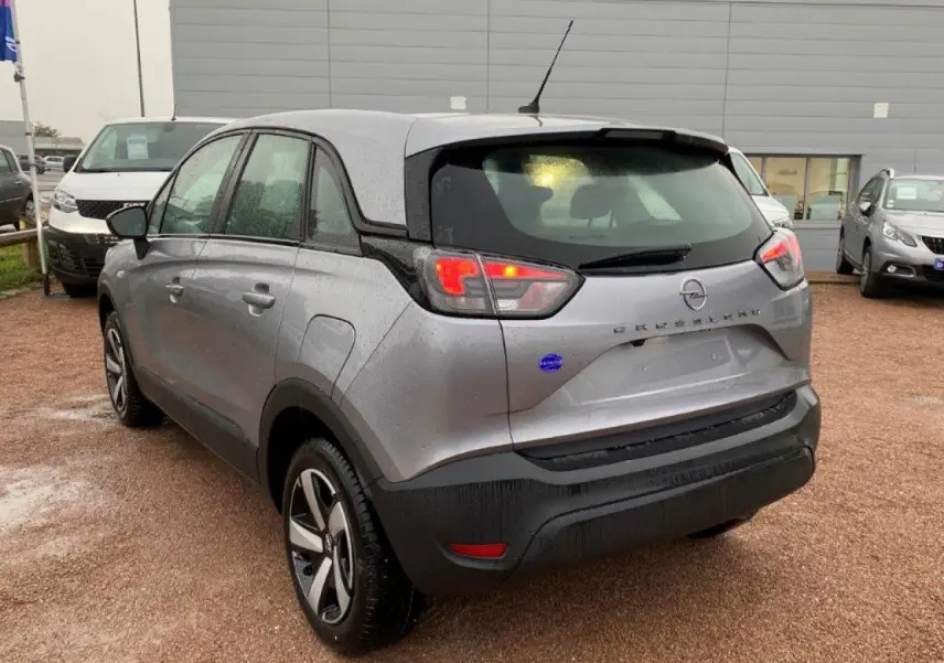 Opel Crossland gris métallisé vu en 3/4 arrière gauche sous la pluie, avec feux arrière allumés et jantes bicolores.