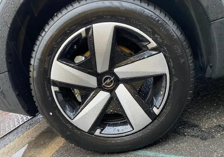 Gros plan sur la roue avant gauche de l’Opel Crossland gris métallisé avec jante alliage bicolore et gouttes d’eau visibles.